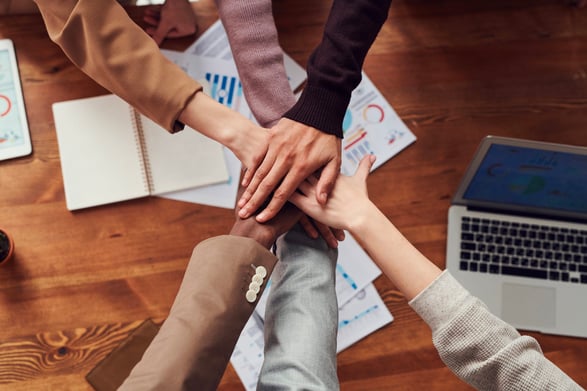 diverse team of people putting hands together over a pile of data sheets